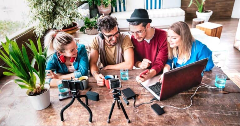 A group of marketing professionals sit at a desk surrounded by a laptop, camera, and microphone.